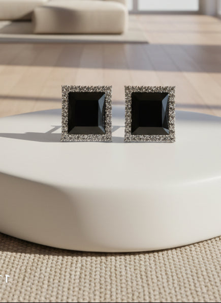Pair of black square earrings with silver frames on a wooden surface